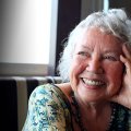 a grey-haired woman smiles resting her head on her hand